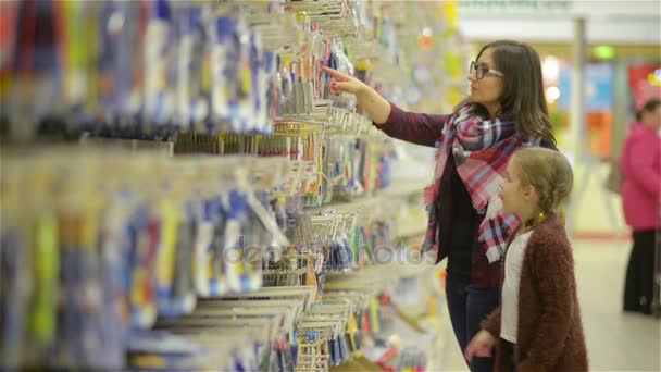 Madre joven con un niño dentro del supermercado Elección de bienes. Niña señala el dedo a algo y mamá permite comprarlo y poner en la cesta roja — Vídeos de Stock