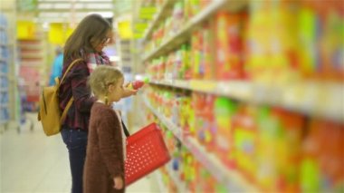 Evli ve sevimli kız süpermarket mal ile raf yakınındaki ayakta. Anne ile çocuk alışveriş bir mağazada suyu bölümünde birlikte.