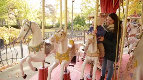 Mom and Child Riding on the Carousel in the Park. Smiling Mother and Little Daughter Spend Time Together Outdoors During a Sunny Autumn Day on Roundabout — Stock Video