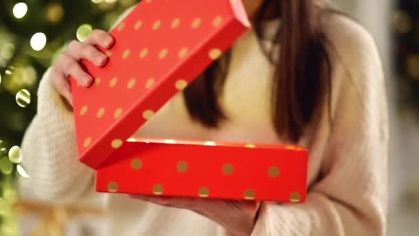 Frauenhände öffnen zu Hause rote Schachteln. bis zur Unkenntlichkeit brünett Eröffnung Weihnachtsgeschenk. verschwommene Weihnachtsbeleuchtung auf Hintergrund. — Stockvideo