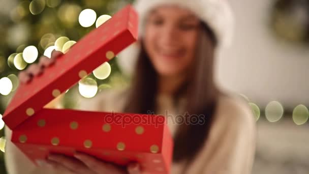 Csinos nő Santa kalap meglepett a meglepetés belsejében a piros mezőbe. Aranyos mosolygós lány karácsonyi ajándék karácsony fa háttér, Vértes megnyitása. — Stock videók