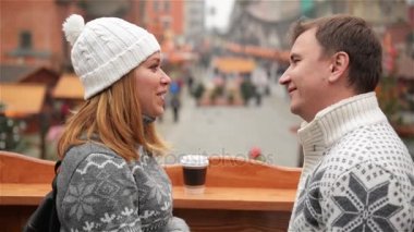 Yakışıklı adam ve Noel Pazar arka plan üzerinde kahve ile yüz yüze kalan güzel kadın. Çift konuşmak ve seyir aşık Xmas tatil sırasında antik şehrin meydanında.