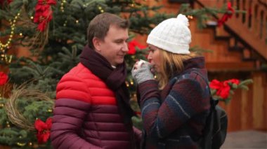 Güzel kadın gelenek Noel pazarında kahve içme ve yakışıklı erkek. Karı ve koca birbirlerine sevgi ve hassasiyet ile sıcak bir içecek açık havada Xmas ağacı arka plan üzerinde geçiriyorum bakın.