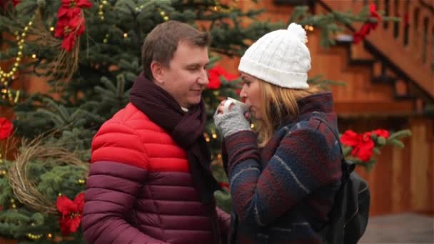 Pohledný muž a Pretty Woman, pití kávy na tradici vánočního trhu. Manželka a manžel se na sebe s láskou a něhou venku s teplý nápoj na vánoční strom pozadí. — Stock video