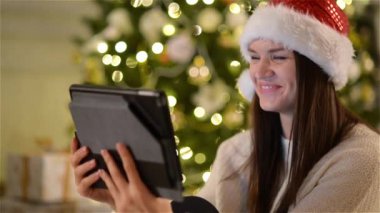 Noel Baba şapkası muhteşem Bayan biri Video kamera kullanarak Tablet üzerinde Xmas ağacı arka plan Noel'de kutlama sırasında derse.