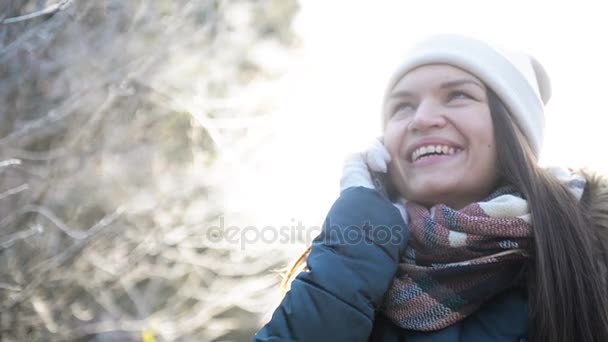 Morena bonita usando Smartphone ao ar livre em tempo de inverno gelado. Garota sorridente conversando com alguém pelo telefone celular de pé no parque na manhã ensolarada. Natureza Contexto . — Vídeo de Stock
