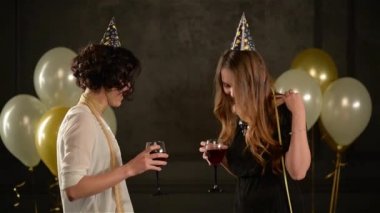 Şampanya ve şarap birbirinizle hava balonları siyah zemin üzerine konuşmak ile gözlük tutan iki kız arkadaşım. Güzel kadın doğum günü partisinde kapaklar ve elbiseler giyen görüşme.