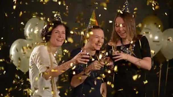 Vrolijke jonge vrouwen gelukkige verjaardag willen hun vriend onder gouden Confetti. Schattige meisjes vieren op een feestje houden in handen glazen van Champagne en wijn, klatergoud vallen van bovenaf. — Stockvideo