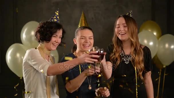 Három nő szemüveg csengő és nevető élvezze születésnapi Party között arany konfetti. Fiatal hölgy szórakozni sapkát visel, és némi alkoholt ünnepe.