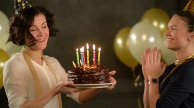 Mumlar ve çalışıyorum bir çikolatalı kek ısırık bir parçasını kapalı tutan doğum günü kızı. Güzel Bayan ile birlikte altın ve beyaz hava balonları siyah zemin üzerine kutluyor onun arkadaşı.