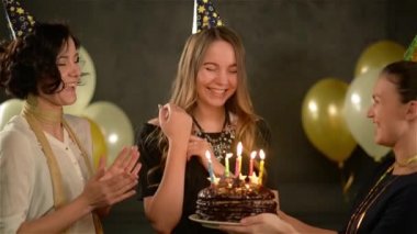 İyi ki doğdun şarkı onların arkadaşı ve çikolatalı pasta vererek kapaklar iki kadınlar. Şaşırtıcı Bayan darbeler mumlar kutlama sırasında. Siyah arka plan ile altın ve beyaz hava balonları.