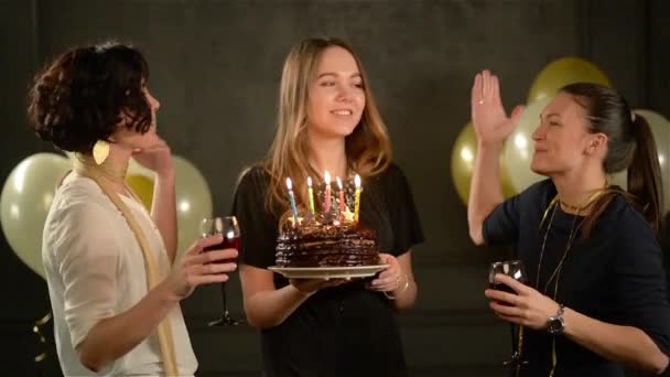 La giovane bella donna fa un desiderio e spegne le candele sulla torta al cioccolato, due sorridenti signore che battono gli occhiali con vino rosso. Ragazza di compleanno con i suoi amici durante la celebrazione . — Video Stock