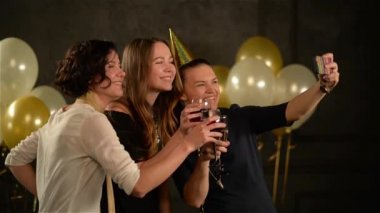 Arkadaşlar elinde Selfies gözlüklü alarak bir partide grup. Gülümseyen kadın beyaz ve altın hava balonları siyah zemin üzerine cep telefonuyla doğum günü kutlamaları sırasında eğlenin.