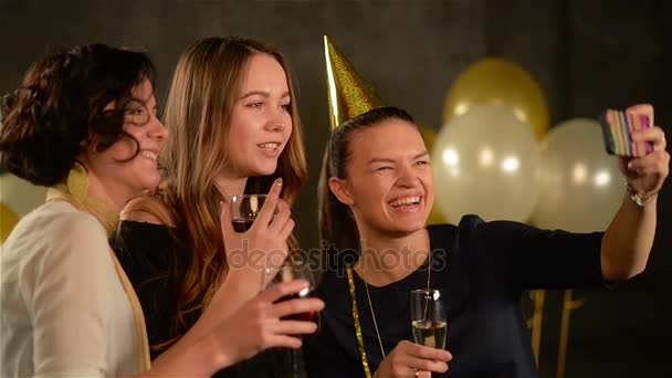 Digitaal Gadget lachende meisjes gebruiken om een foto op een feestje op zwarte achtergrond met lucht ballonnen. Jonge vrouwen met glazen lachen Smartphone scherm kijken tijdens de viering van de verjaardag. — Stockvideo