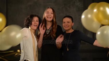 Üç kız altın ve beyaz balonlar gizlemek sonra aniden ortaya ve yaygın olarak kamera seyir gülümse. Siyah arka plan üzerine stüdyoda eğleniyor kadınlar heyecanlı.