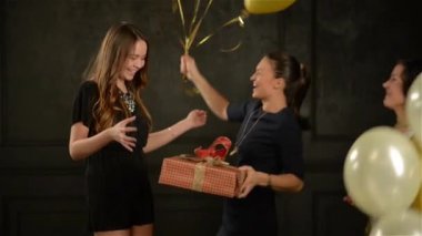 Ona bir hediye vermek için bir arkadaş sarılma uzun saçlı genç sevimli kız. İki gülümseyen kadın tutarak balon grup. Siyah arka plan.