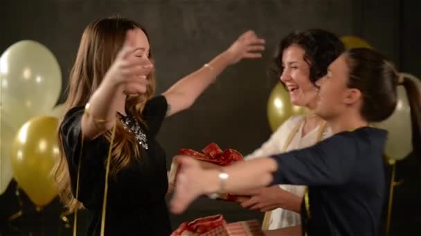 Două femei încântate își felicită prietenul îmbrățișându-o și oferindu-i cadouri. Fata de naștere a primit cutii cu cadouri. Fundal negru cu baloane cu aer alb și auriu . — Videoclip de stoc