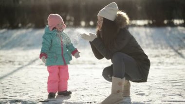 Genç anne onun elinde kar üzerinde üfleme, küçük kızı kar taneleri üzerinde arıyor. Kış sabahı soğuk güneşli havalarda açık havada oynayan kız çocuğu olan kadın.