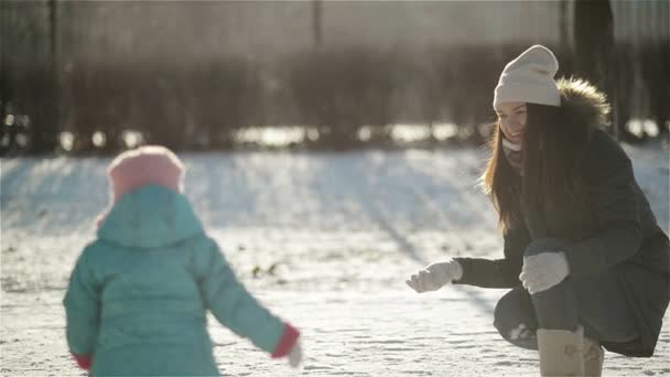 年轻的妻子是在她的宝宝玩外面扔雪球在冬天。母亲和女儿都享受着寒冷晴朗早晨室外. — 图库视频影像