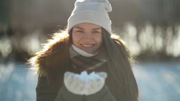 Радостная женщина убирает снег из рук, развлекаясь на улице в холодную погоду по утрам. Симпатичная девушка играет в парке в зимнее время . — стоковое видео