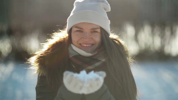 Mulher alegre bonita está soprando afastado a neve das mãos que se divertem ao ar livre no tempo frio na manhã. Menina bonita brincando no parque no inverno . — Vídeo de Stock