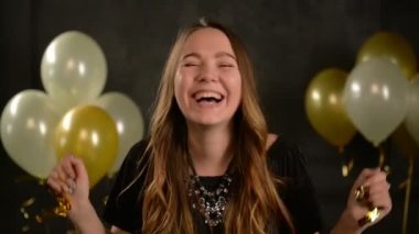 Hava balonları ile siyah arka plan üzerinde ellerini Studio üzerinde altın konfeti ile genç kadın gülüyor. Uzun saçlı ve kolye kutlama sırasında parti kız.