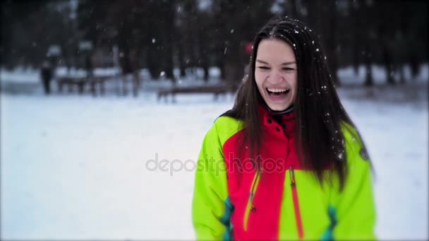 Милая молодая девушка с длинными волосами и прекрасной улыбкой, наслаждающаяся зимой на открытом воздухе. Портрет женщины в разноцветном лыжном костюме, снежинки медленно падают . — стоковое видео