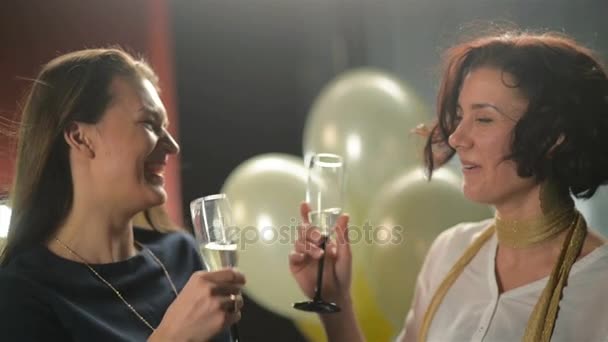 Bonitas morenas están hablando entre sí durante la fiesta de discoteca y tintineando copas con champán. Dos mujeres sonrientes conversan en el club . — Vídeos de Stock