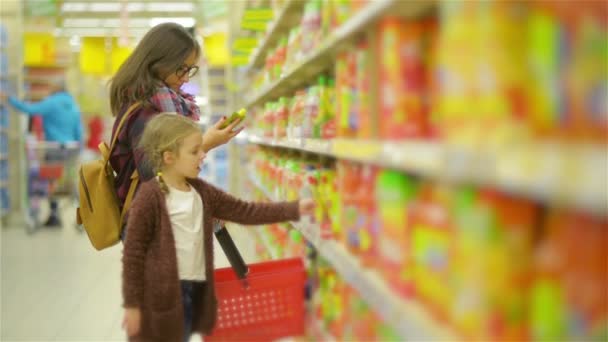 Νεαρή μαμά και το παιδί την αγορά τροφίμων σε ένα σούπερ μάρκετ. Όμορφη γυναίκα με χαριτωμένο κορίτσι στέκεται κοντά στο ράφι με τα αγαθά φαίνεται προσεκτικά κάθε προϊόντα — Αρχείο Βίντεο