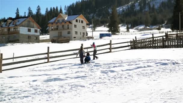 Zwei Freundinnen rollen riesige Schneebälle den Hügel hinauf, und das dritte Mädchen eilt ihnen zu Hilfe. Glückliche Kinder spielen im Winter vor unserer Haustür. — Stockvideo