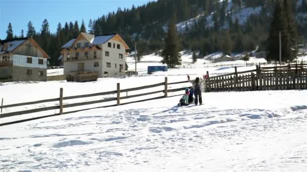 Los niños están jugando juego de invierno juntos al aire libre. Dos niñas y un niño están rodando una gran bola de nieve en la colina durante el clima cálido y soleado . — Vídeo de stock