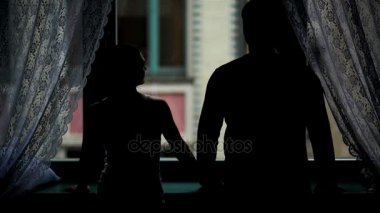 Pencerenin yanında çift Kontrast portresi. Kadın adam el alarak içeri bunlar öpüşme ve sevgi ile Hugging. Karanlıkta genç ailesinin arkadan görünüm.