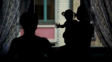 Mutlu aile pencerenin sarılma görünümü geri. Anne, baba ve küçük kızları kucaklayan ve evde gülümseyen iki Ponytails ile silüeti.