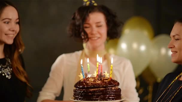 Birthday Girl está celebrando junto con sus dos amigos sobre fondo negro con globos aéreos. Mujer alegre hace un deseo y sopla las velas en el pastel de chocolate . — Vídeo de stock