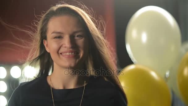 Primo piano Ritratto di bella bruna con i capelli lunghi svolazzanti e sorriso affascinante. Una donna sorridente sta guardando la telecamera. Palloncini d'aria e torce elettriche sfondo . — Video Stock