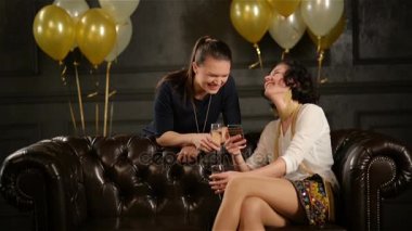 İki esmer kısa portresi closeup ile bardak şampanya elinde bir parti sırasında Giydir. Smartphone kullanarak ve gülen bayanlar vardır.