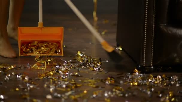 Подметание золотых и серебряных конфетти в конце вечеринки. Красочная бумага на полу. Крупный план женских ног и метлы. Концепция домашнего хозяйства . — стоковое видео