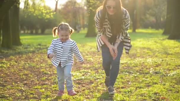 Mãe e filha em roupas listradas estão brincando juntos Aproveitando o clima quente da primavera no parque. Engraçado menina está correndo longe de sua mãe . — Vídeo de Stock