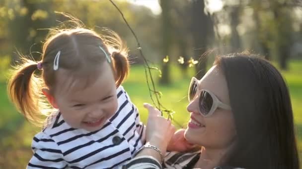 Zbliżenie na zewnątrz portret uśmiechający się matka i córka w parku. Piękna brunetka z okulary jest Holding dziewczynka z dwóch Ponytails śmieszne. — Wideo stockowe