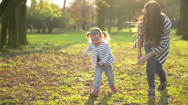 Ein lustiges kleines Mädchen läuft ihrer Mutter davon, die draußen im Park spielt. Aktives weibliches Kind hat Spaß an sonnigem Frühlingstag. — Stockvideo