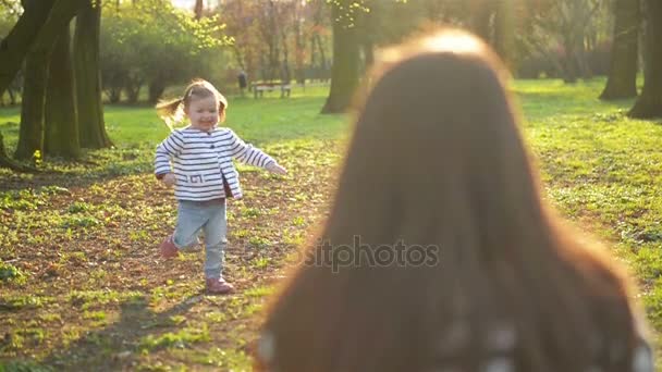 Joyeuse fille active court vers sa mère et l'accueille dans le parc pendant la période printanière. Famille heureuse passer du temps libre ensemble à l'extérieur . — Video