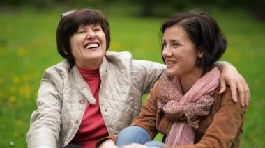 İki gülümseyen esmer kadınlar birbirlerine oturan için paket sırasında piknik Park üzerinde konuşuyor. Yetişkin kızıyla kısa kıvırcık saçları ve annesinin portresi.