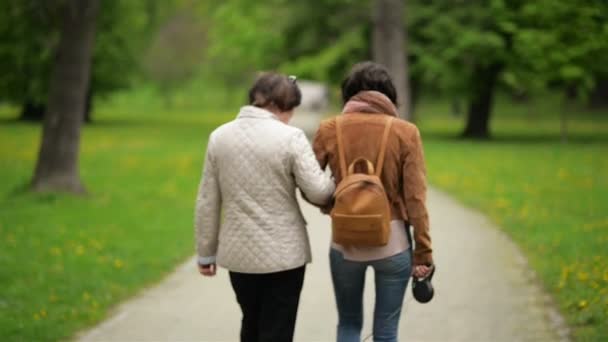 La hija adulta está paseando con su madre y su perrito en el parque. Dos mujeres caminan con su mascota . — Vídeos de Stock