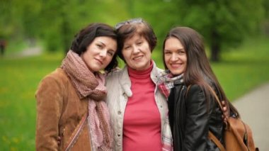 Üç güzel kadın çekici gülümseme ile parkta ayakta açık havada sarılma vardır. Mutlu anne ve iki yetişkin kızı bahar portresi.