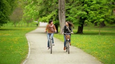 Gülen iki bayan arkadaşlar parkta bisiklet sürme vardır. Birlikte vakit Bisikletleri ile genç komik kadın.
