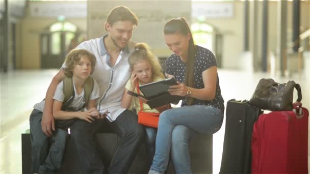Vader en moeder met twee kinderen zitten in de wachtkamer van het Centraal Station of op het vliegveld. Mooie moeder is haar Tablet tonen. Kinderen zijn Smartphones in hun handen houden. — Stockvideo