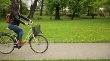 İki güzel esmer baharda üzerinde bisiklet bir sonra başka bir şehir parkta biniyor. Sevimli genç kadınlarda kot pantolon, ceket ve eşarp bisiklet ile harcama zaman açık havada vardır.