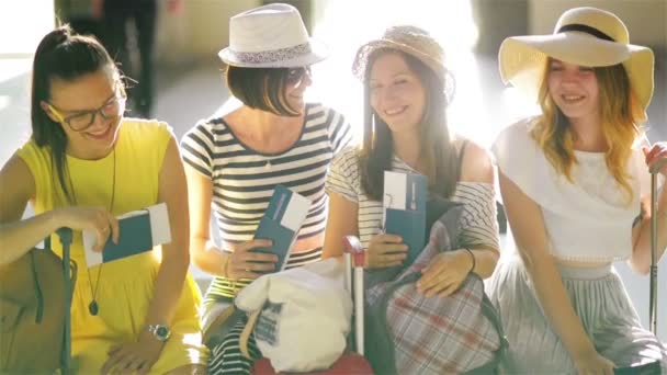 Cuatro morenas vestidas con ropa de verano están sentadas en la sala de espera del aeropuerto con pasaportes y entradas en las manos . — Vídeo de stock