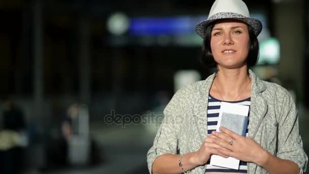 Portrait de jeune brune aux cheveux courts, chapeau d'été et robe rayée montrant son passeport et son billet à la caméra de l'aéroport. Tableau de bord flou sur le fond . — Video