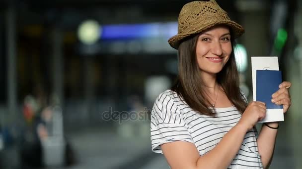 Attraktive junge Frau mit Sommermütze wartet so glücklich mit Ticket und Pass in der Hand auf ihr Flugzeug am Flughafen. — Stockvideo